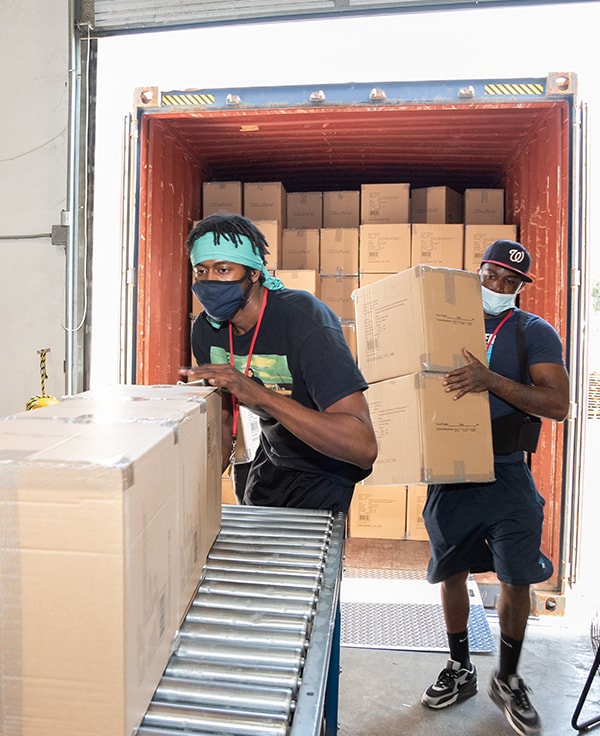 Two AMS Fulfillment employees loading boxes into a warehouse from an open truck