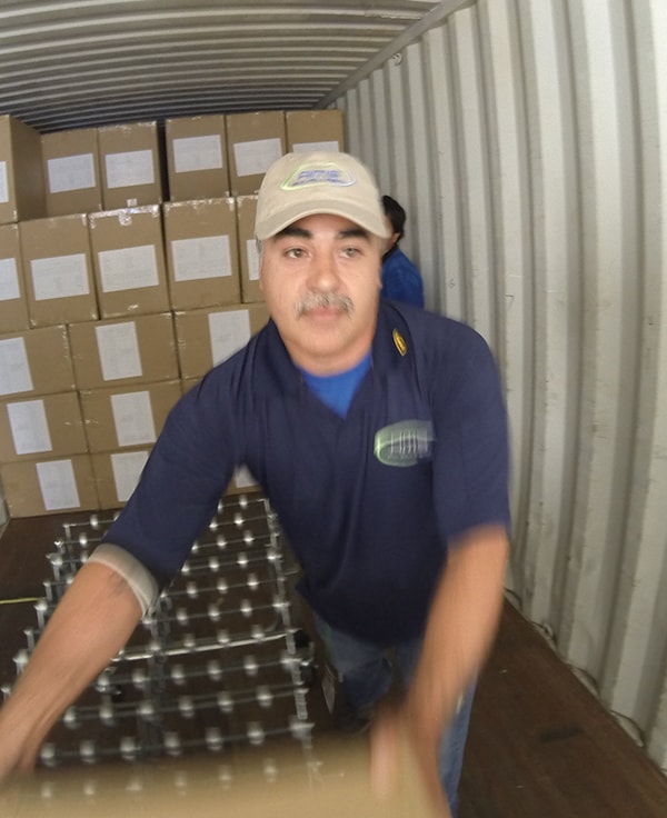 Employees in blue shirts working in a warehouse, handling boxes and placing them on various conveyor belts for transport