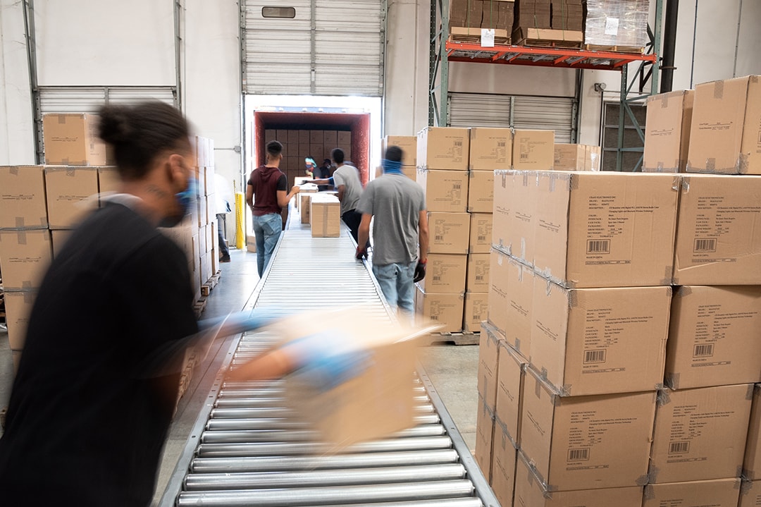 Several AMS Fulfillment employees loading boxes into a warehouse from an open truck