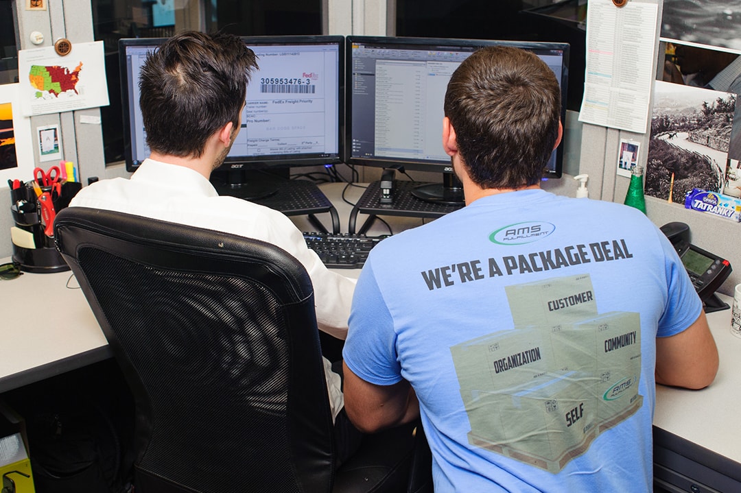 Behind view of two employees sitting a desk looking at computer screen monitors