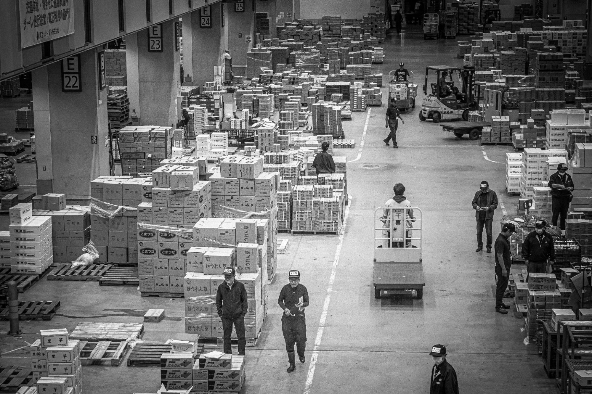 A black and white image of a warehouse, where workers are shown organizing, moving, and managing a large volume of packaged goods and boxes throughout the facility.