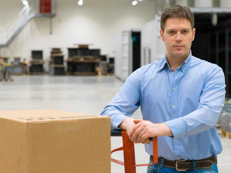 An AMS worker standing next to a dolly with boxes.