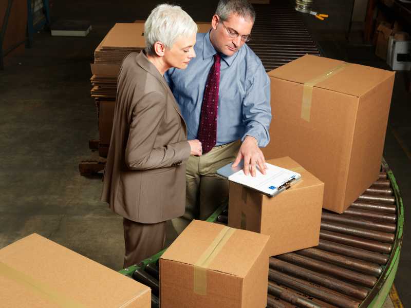 AMS managers looking at packages and a clipboard on a conveyor belt.