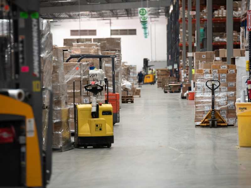 A warehouse aisle with multiple palettes of goods on forklifts, ready to be shipped. 	