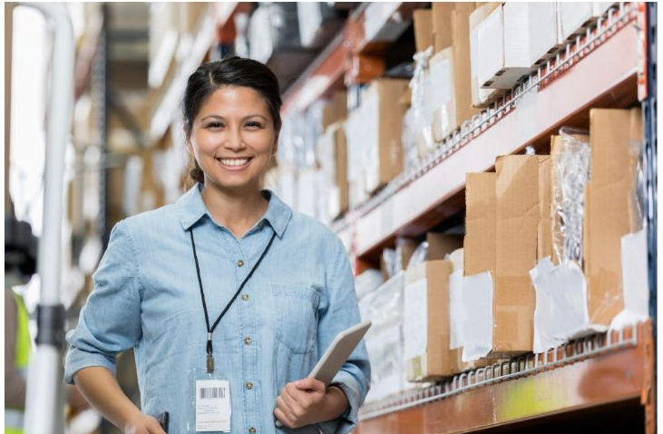 A person standing next to a shelf of items ready to be shipped. 	