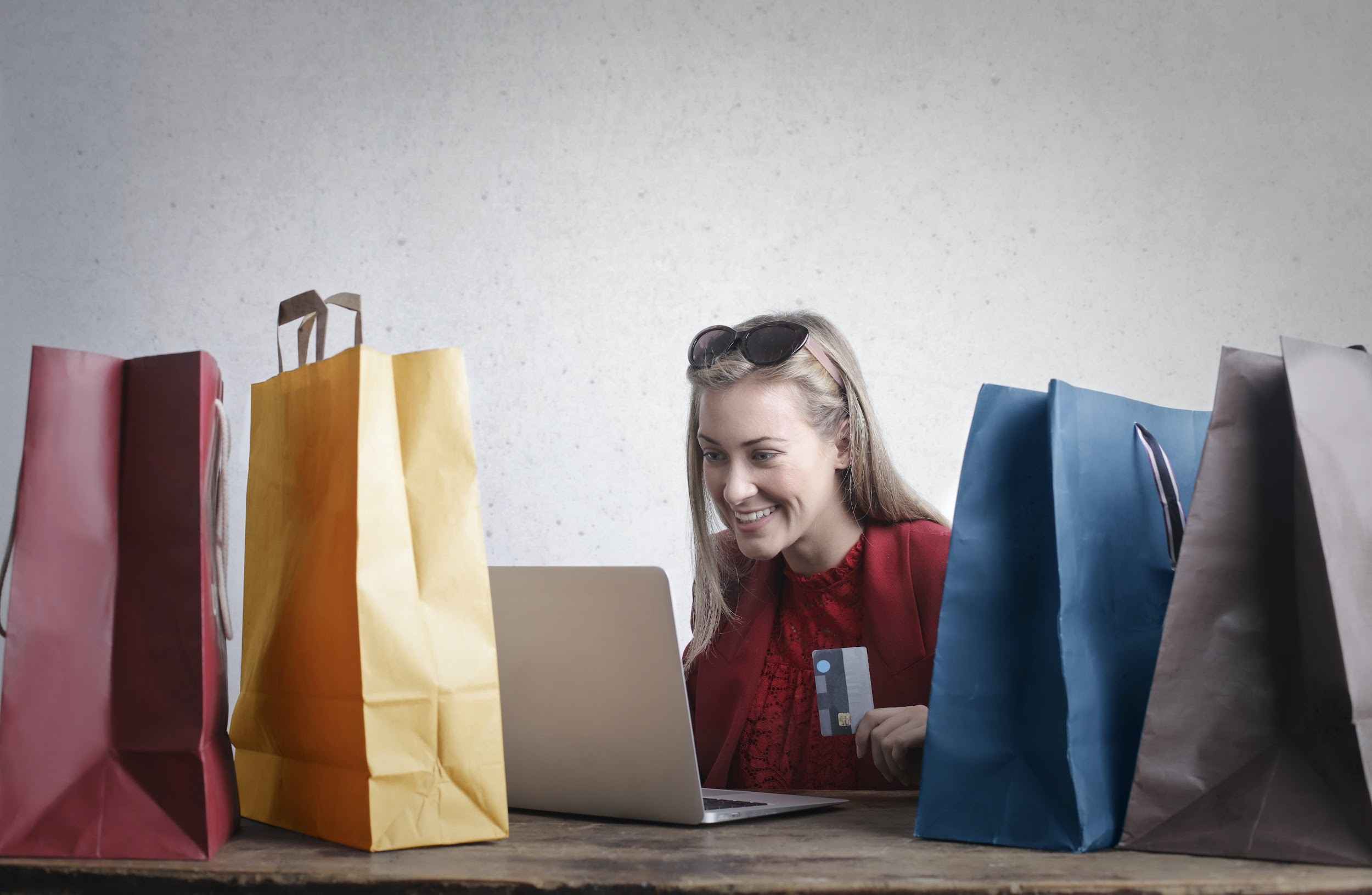 lady in red shirt on a macbook with a credit card surrounded by colorful bags - AMS Fulfillment