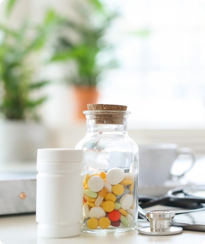 Clear glass jar with a cork top, filled halway with various supplements, next to an all-white, plastic container.