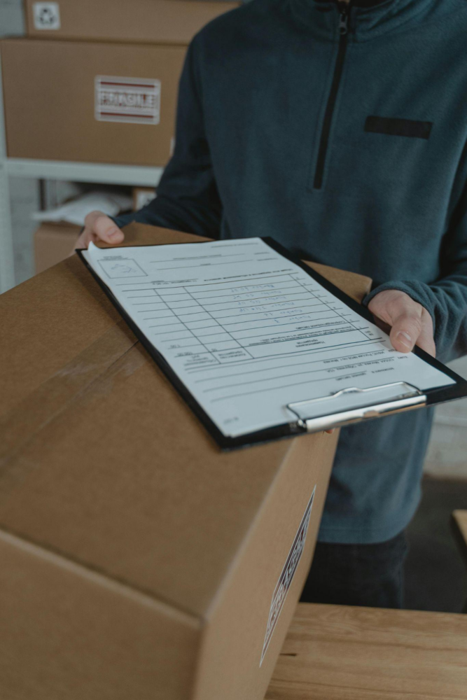 A person holds a clipboard and boxes at at Fulfillment Center – AMS Fulfillment