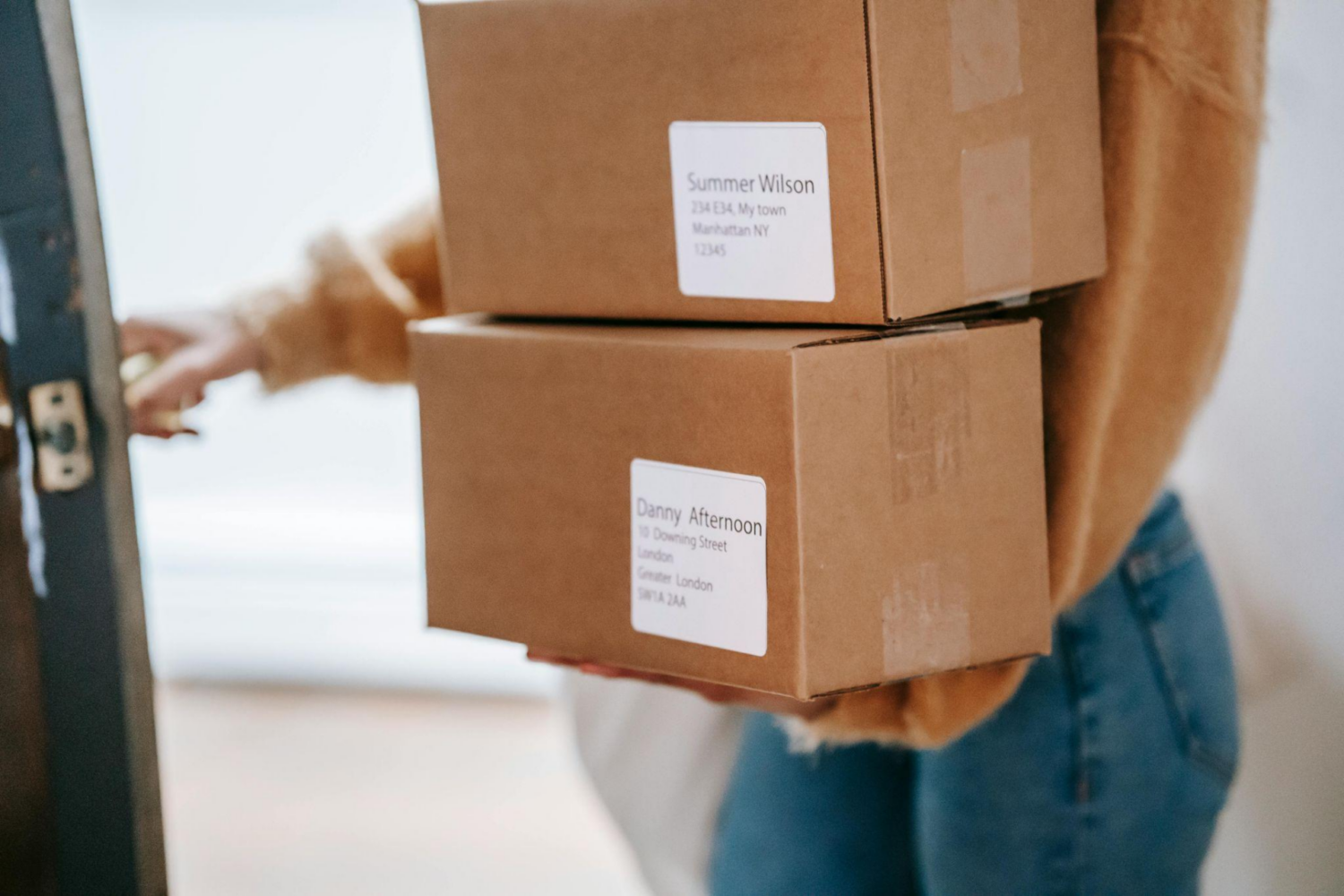 A person holding delivery boxes while opening a door.