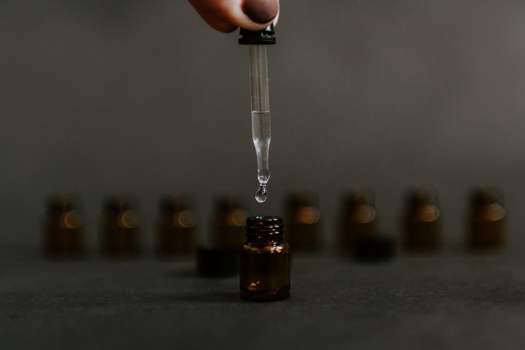 A dropper putting liquid into a small, glass container, with several other containers in the background.