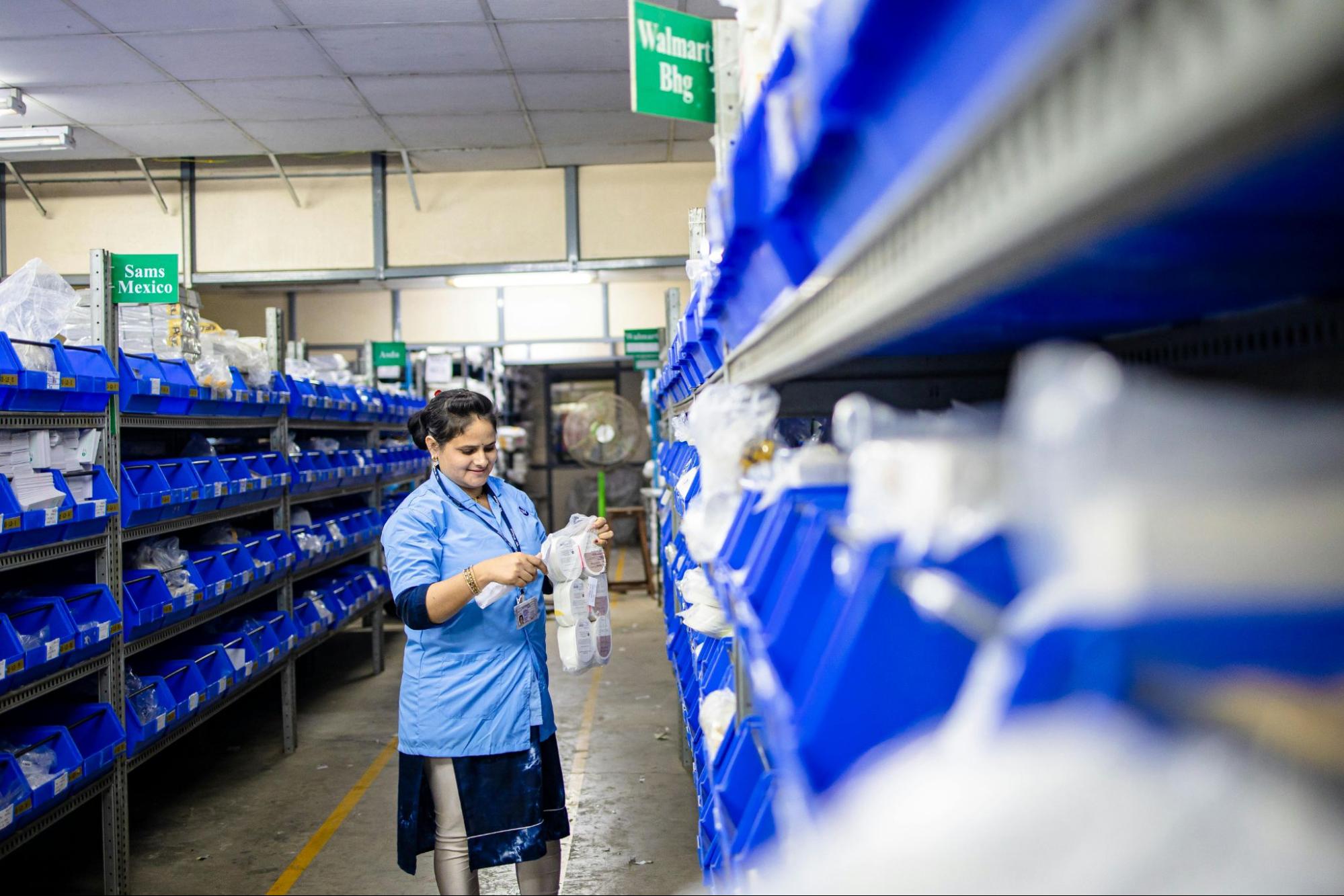 A person is checking an item after taking it off a shelf of blue bins.