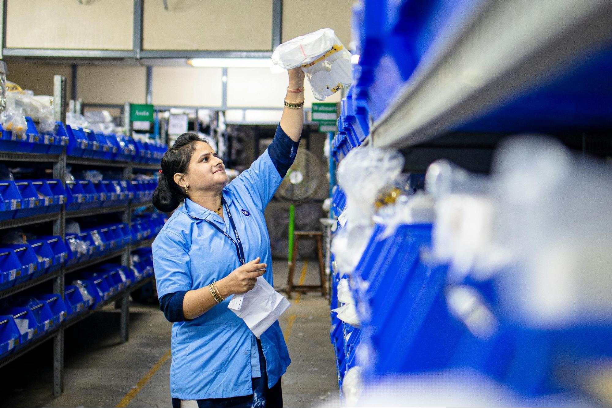 A person is picking an item from a shelf of blue bins.
