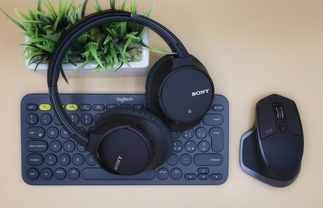 A pair of headphones is lying on a keyboard and a fake plant, with a computer mouse to the right of them.