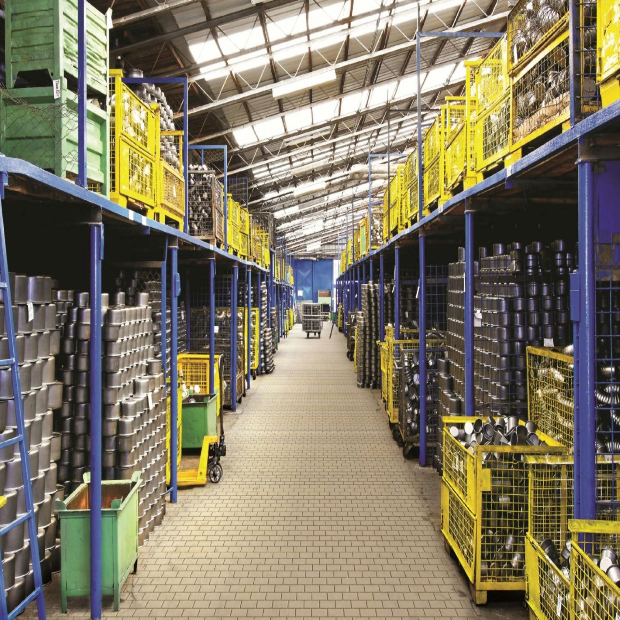 A long, well-organized warehouse aisle, featuring tall industrial blue metal shelving units on both sides, which are stocked with various products.