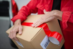 A person in a red jacket is sealing a package with red duct tape.