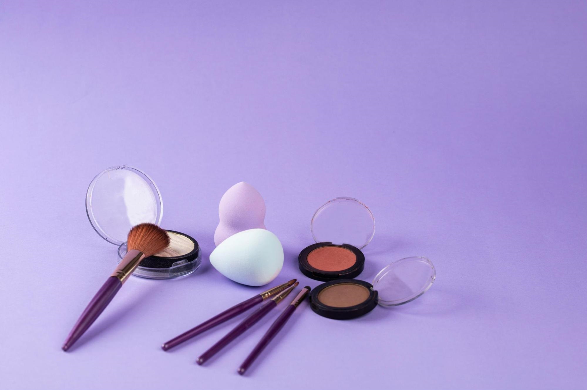 Various makeup products and brushes against a purple background.