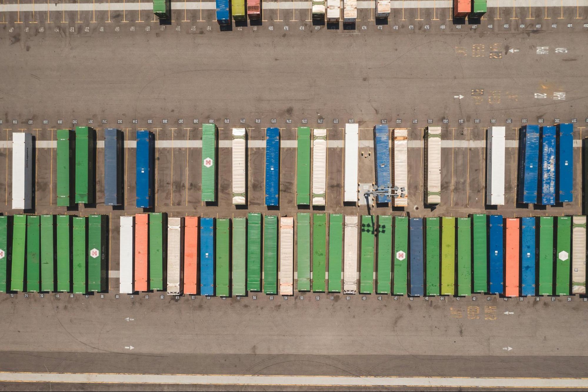 An aerial, overhead view of a shipping container terminal, with multiple rows of shipping containers.
