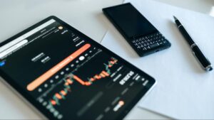 A phone, pen, and a tablet with data charts on it are sitting on a white table.