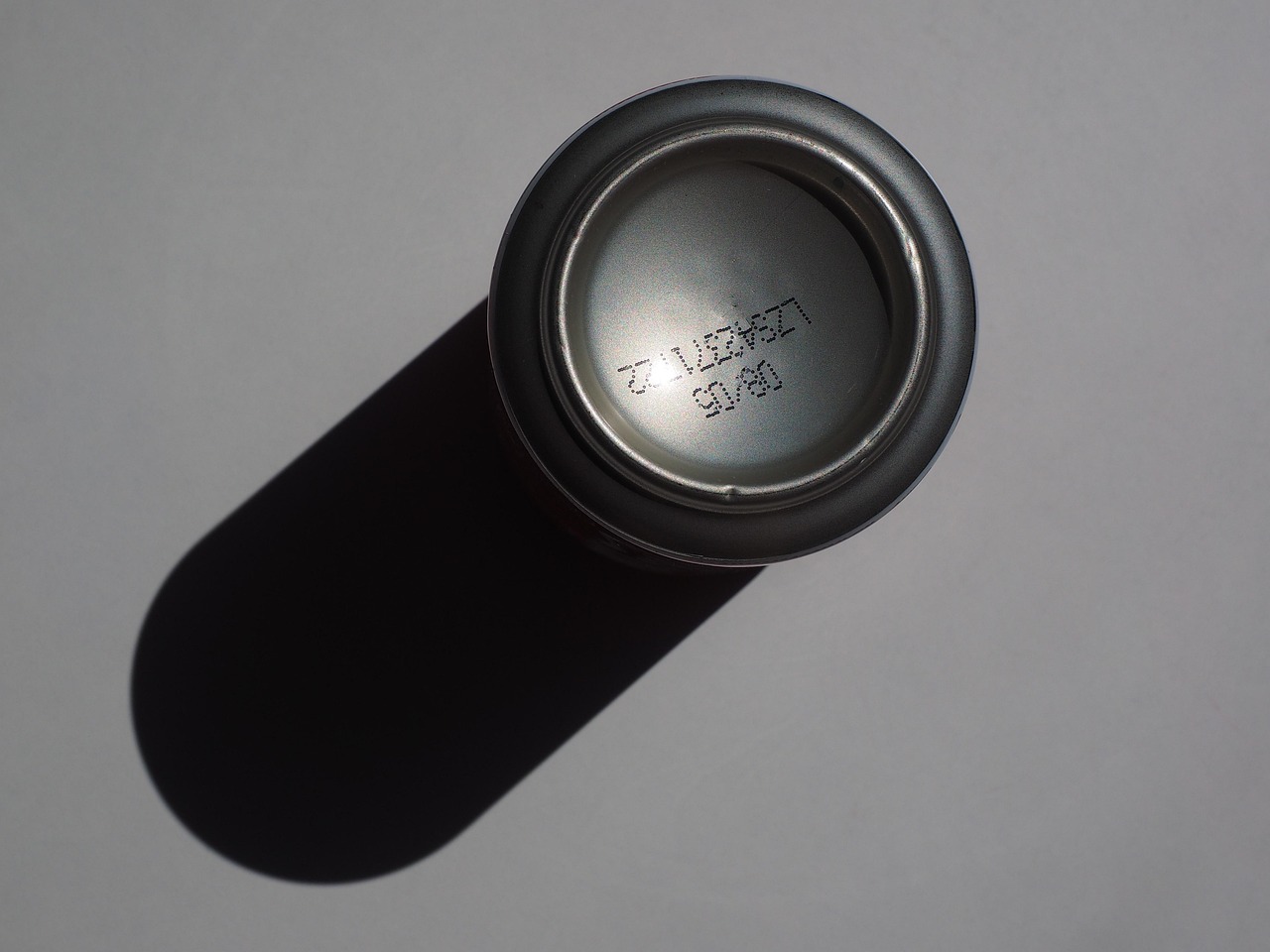An image of the bottom of a soda can, with the can casting a shadow to the right.