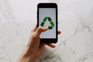 A hand is holding a cellphone which is showing a green recycling logo on it.