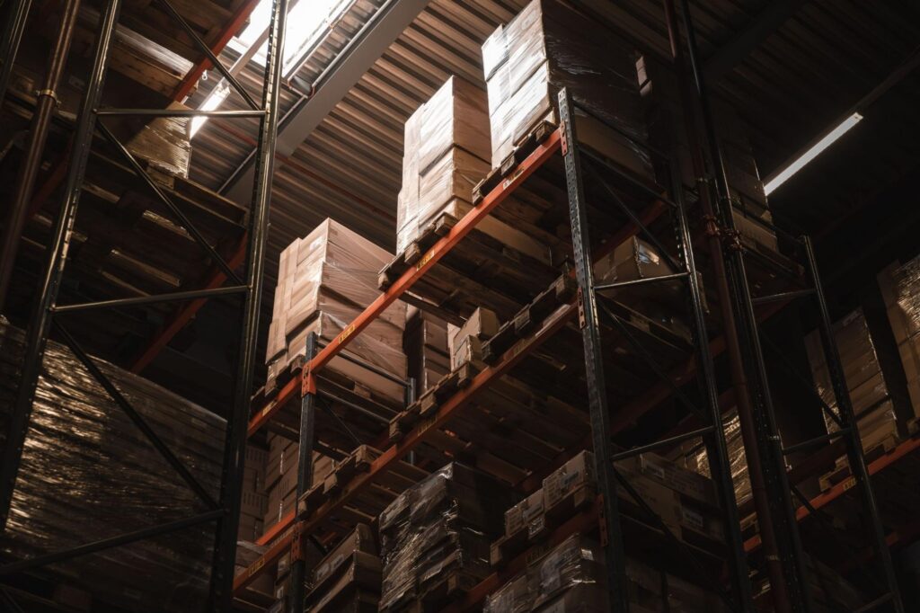 Tall industrial warehouse racking filled with stacked, shrink-wrapped pallets viewed from below.