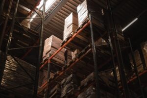 Tall industrial warehouse racking filled with stacked, shrink-wrapped pallets viewed from below.