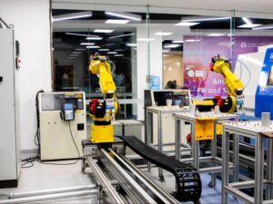 Two bright yellow industrial robotic arms mounted on metal linear tracks inside a modern manufacturing facility or training lab.