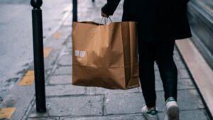 An image of a person walking with a brown retail shopping bag.